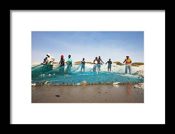 Working Framed Print featuring the photograph Fishermen pulling the net at the beach. by Peeterv