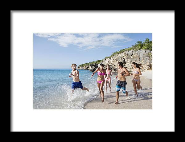 Young Men Framed Print featuring the photograph Group of friends running together along sandy beach by Felix Wirth