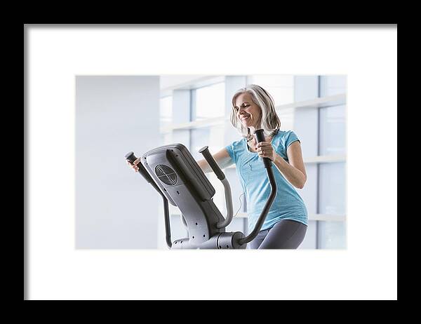 55-59 Years Framed Print featuring the photograph Happy Caucasian woman on elliptical trainer at gym by Mike Kemp