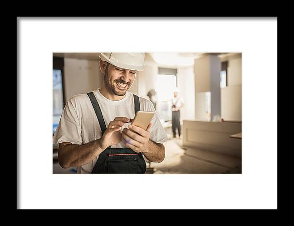 Expertise Framed Print featuring the photograph Happy construction worker using cell phone during home renovation. by Skynesher