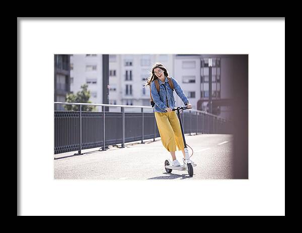 Environmental Conservation Framed Print featuring the photograph Happy young woman riding electric scooter on a bridge by Westend61