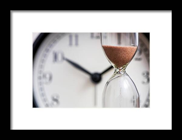 Color Image Framed Print featuring the photograph Hourglass on the background of office watch as time passing concept for business deadline, urgency and running out of time. Sand clock, business time management concept by Andrii Zorii