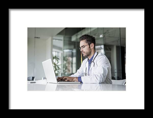 Expertise Framed Print featuring the photograph Male doctor using laptop at desk in clinic by Portra