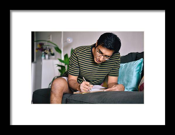 Mental Health Framed Print featuring the photograph Man writing in a diary sitting on a sofa by Mayur Kakade