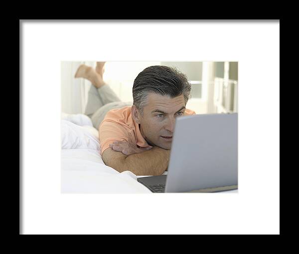 40-44 Years Framed Print featuring the photograph Mature man lying on bed looking at laptop computer, close-up by Matthias Heitmann
