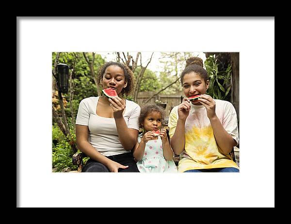 Diversity Framed Print featuring the photograph Mixed-race sisters eating watermelon in backyard. by Martinedoucet