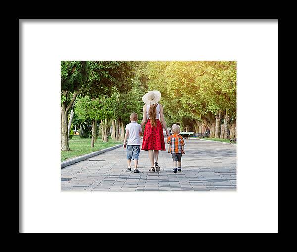 Child Framed Print featuring the photograph Mum and two sons walking in the park, sunny day. View from the back by SomeMeans