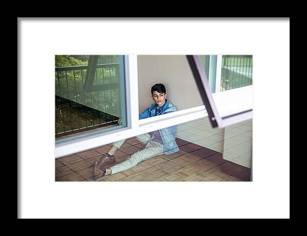 Young Men Framed Print featuring the photograph Portrait of a young man sitting at a wall and looking outside through window by Attila Csaszar
