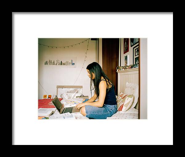 Asian And Indian Ethnicities Framed Print featuring the photograph Profile Shot Of Teenage Girl In Her Bedroom, Working On Laptop by Alys Tomlinson