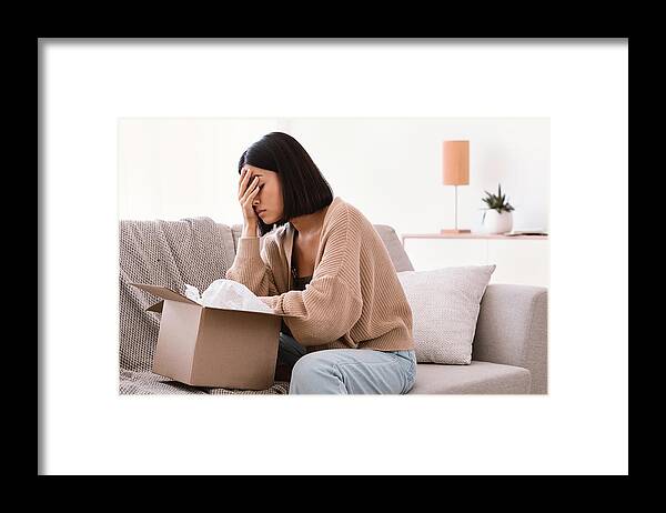 Damaged Framed Print featuring the photograph Sad young lady unpacking wrong parcel, delivery mistake by Prostock-Studio