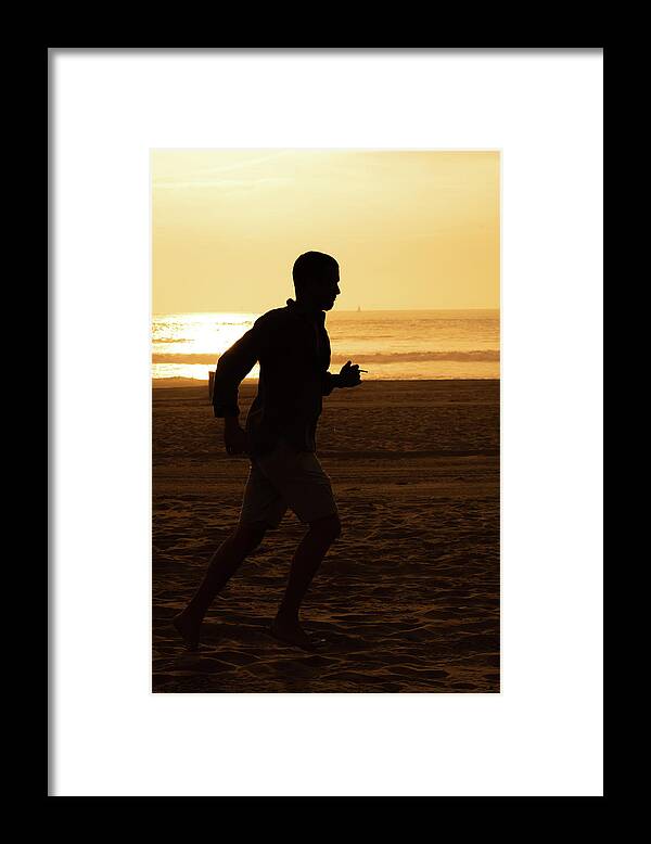 Silhouette Framed Print featuring the photograph Silhouette of a tall man running on beach at sunset stock photo by Mark Stout