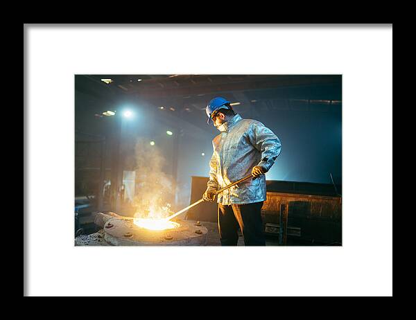 Working Framed Print featuring the photograph Steel worker in protective clothing raking furnace in an industry by RainStar
