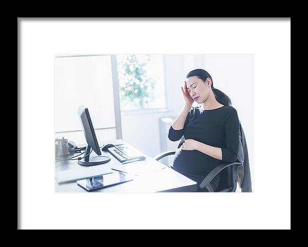 Horizontal Framed Print featuring the photograph Tired pregnant Japanese businesswoman at desk by JGI/Tom Grill