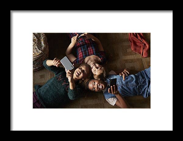 Adolescence Framed Print featuring the photograph Top view of 3 tween girls laughing and looking at their smartphones by Klaus Vedfelt