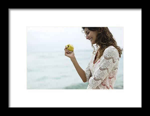 Water's Edge Framed Print featuring the photograph Woman eating apple at the beach by PhotoAlto/Antoine Arraou