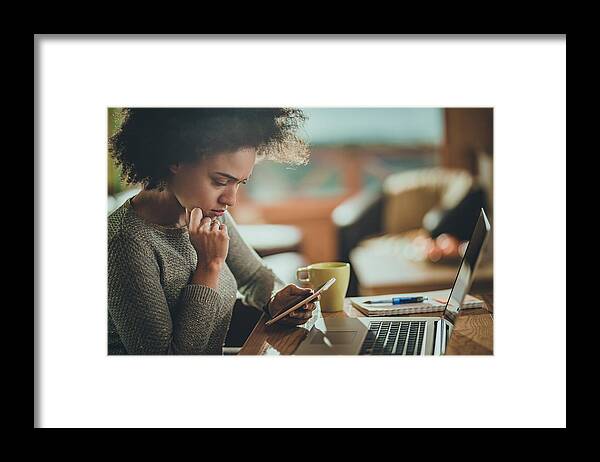 People Framed Print featuring the photograph Worried African American woman using cell phone while working at home. by Skynesher