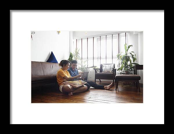 Using Computer Framed Print featuring the photograph Young Chinese couple sitting on the floor at home with a laptop by Carlina Teteris