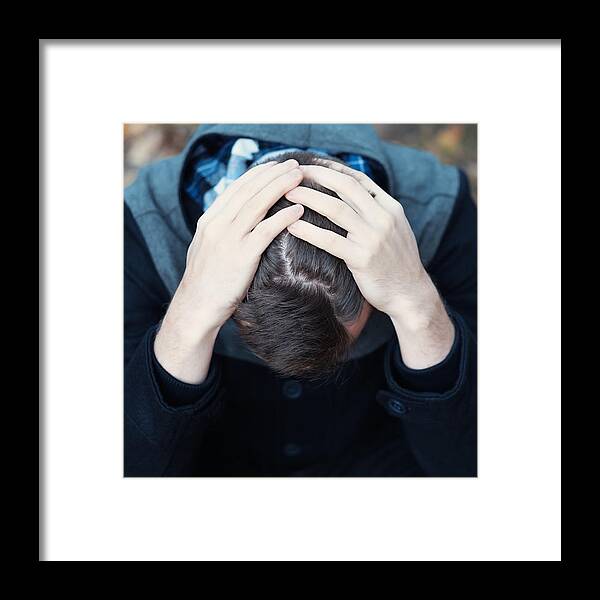 Problems Framed Print featuring the photograph Young man covers his face with his hands in grief by Koldunova_Anna