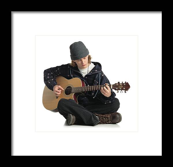 White Background Framed Print featuring the photograph Young Man Wearing A Gray Hat Jacket And Dark Pants Sits On The Ground While Playing A Guitar by Photodisc