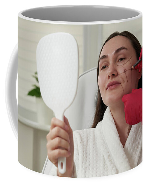 Face Coffee Mug featuring the photograph Cosmetologist using facial marker on patient face before beauty treatment in spa salon by Maria Kray