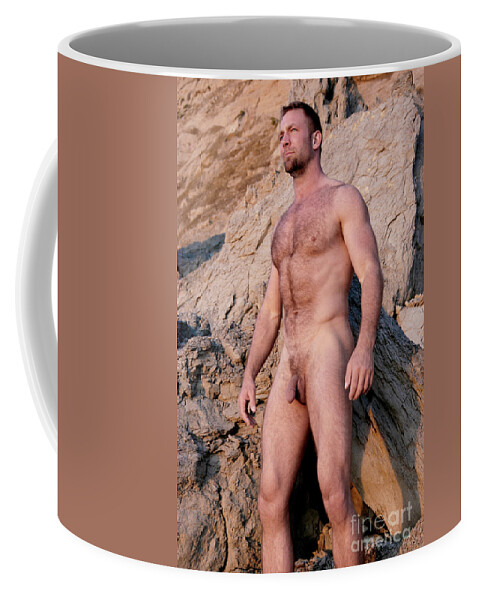 Nude Coffee Mug featuring the photograph Naked man with muscles and a hairy body stands in front of rocks. by Gunther Allen