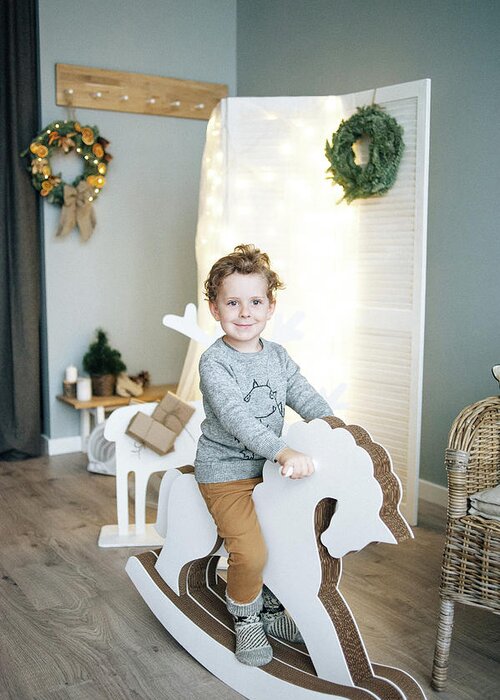 Christmas Greeting Card featuring the photograph Little Boy Sitting On Wooden Horse In Christmas Decorated Room. by Cavan Images