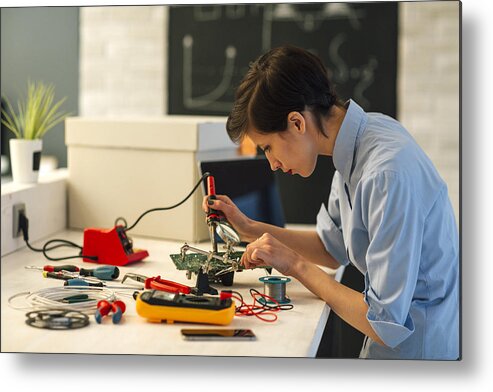 Expertise Metal Print featuring the photograph Woman Soldering a circuit board in her tech office. #1 by Vgajic