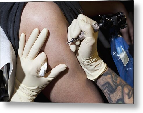Expertise Metal Print featuring the photograph A tattoo artist preparing to tattoo a man's bare arm, close-up by Halfdark