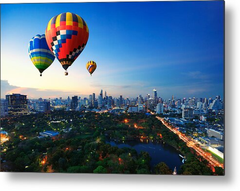Skyline Trail Metal Print featuring the photograph Hot air balloons fly over cityscape at sunset background by Busakorn Pongparnit