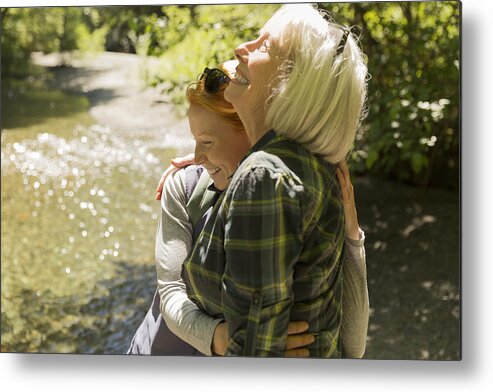 Plaid Shirt Metal Print featuring the photograph Senior woman and daughter hiking hugging by river by Compassionate Eye Foundation/Steven Errico