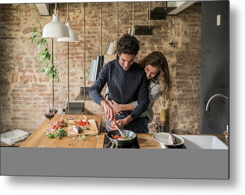 Young Men Metal Print featuring the photograph Young couple cooking fish cuisine at kitchen counter hob by Arno Images
