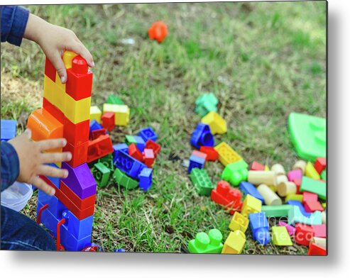 Activity Metal Print featuring the photograph Child playing with colorful blocks sitting on the ground of a garden in spring, negative space. by Joaquin Corbalan