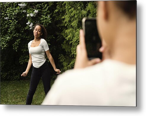 Sibling Metal Print featuring the photograph Mixed-race teenage sisters filming with mobile phone in backyard. #1 by Martinedoucet