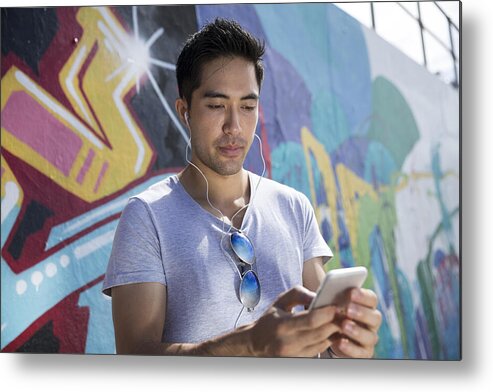 Cool Attitude Metal Print featuring the photograph Asian man in front of graffiti reading phone. by Jenner Images