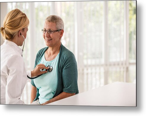 Expertise Metal Print featuring the photograph Doctor using stethoscope while examining patient by Fotostorm