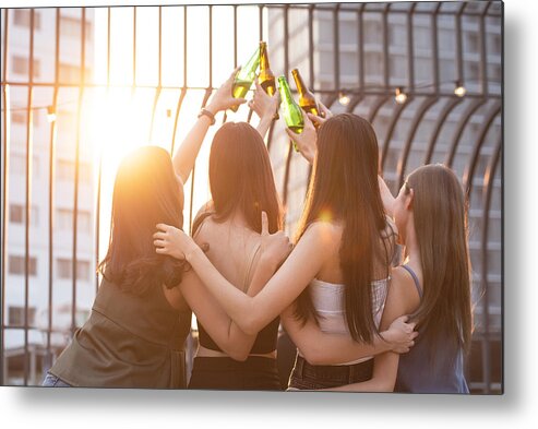 Celebration Metal Print featuring the photograph Group of happy beautiful young asian woman friends on back or rear side raised hand hold bottle of beer dance and toast together on outdoor rooftop terrace in evening of outdoors club. by Mkitina4