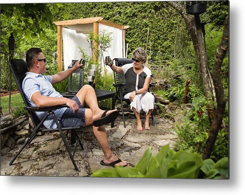 Heterosexual Couple Metal Print featuring the photograph Senior couple having a drink in backyard. by Martinedoucet