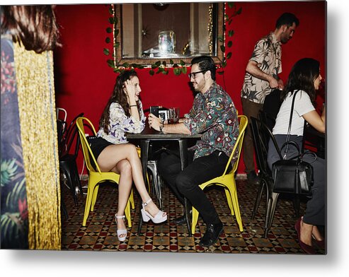 Young Men Metal Print featuring the photograph Smiling couple in discussion while seated at table in night club by Thomas Barwick