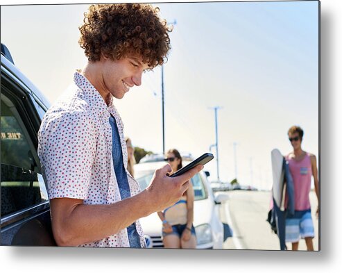 Young Men Metal Print featuring the photograph Smiling young man at a car checking his cell phone by Westend61