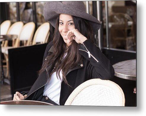Fedora Metal Print featuring the photograph Smiling young woman sitting at a sidewalk cafe. by Jean-Marc PAYET