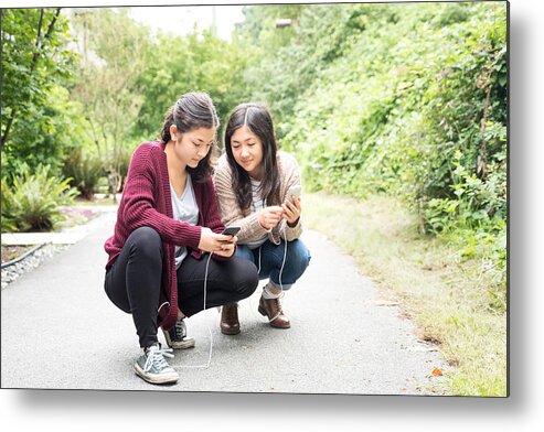 Outdoors Metal Print featuring the photograph Teenaged Eurasian Sisters Playing Augmented Reality Games on Smartphones by PamelaJoeMcFarlane