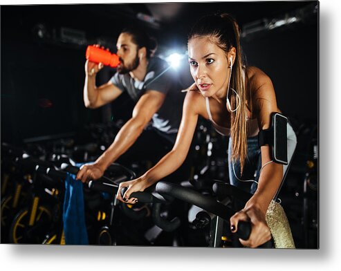 Young Men Metal Print featuring the photograph Two young people exercising on exercise bike at gym by EmirMemedovski