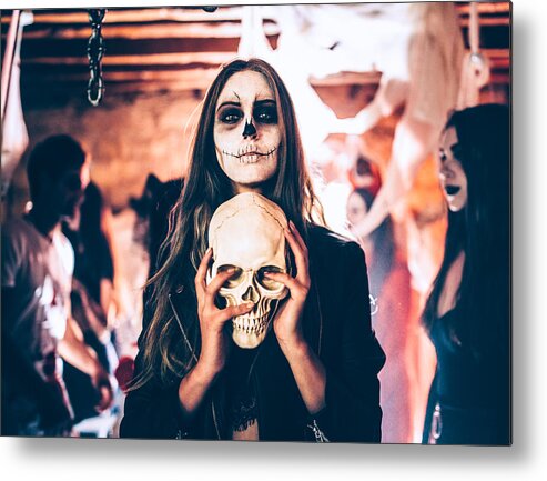 Young Men Metal Print featuring the photograph Young woman with skeleton make-up holding skull at Halloween party by Wundervisuals