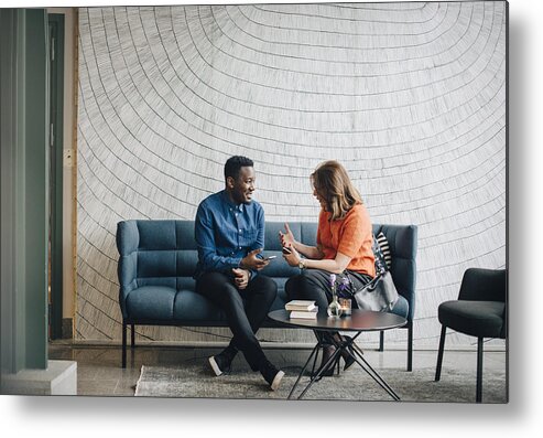 Young Men Metal Print featuring the photograph Businessman and woman taking while sitting on couch against wall at conference by Maskot