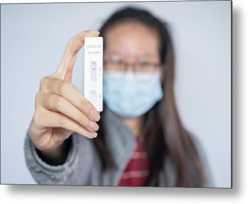 Protective Face Mask Metal Print featuring the photograph Asian woman holding a rapid antigen test pad after testing result is negative. by Boy_Anupong