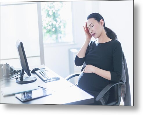 Horizontal Metal Print featuring the photograph Tired pregnant Japanese businesswoman at desk by JGI/Tom Grill