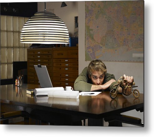 People Metal Print featuring the photograph Man playing with model motorcycle at desk in office by Michael Blann