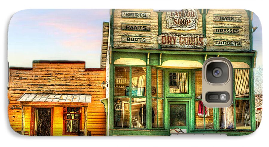 Virginia City Dry Good Store. Merchantile. Vintage Archetecture. Buildings. Sled. Wheelbarrow. Vintage Dresses. Wool Spinners. Lady Clothing. Children Clothing. Mens Clothing. Photography. Fine Art. Canvas. Texture. Hdr. Print. Digital Art. Poster. Greeting Card. City Scene. Cloudy Skies. Fence. Galaxy S7 Case featuring the photograph Virginia City Dry Goods by Mary Timman
