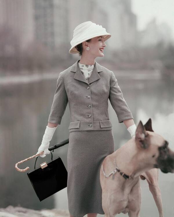 Fashion Accessories Animal Outdoors Daytime Front View One Person People Female Model Young Woman Young Adult Young Adult Woman Looking Away One Animal Animals Dog Domesticated Animal Pet Smiling Hat Headgear Purse Bag Blazer Jacket Skirt Gloves Umbrella Glamour Great Dane 1950s Style 20-24 Years 20s Adult #condenastvoguephotograph February 1st 1956 Poster featuring the photograph A Model Wearing A Gray Suit With A Dog by Karen Radkai