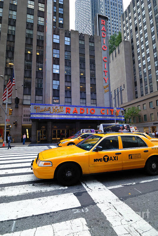Building Poster featuring the photograph Yellow Cabs pass in front of Radio City Music Hall by Amy Cicconi